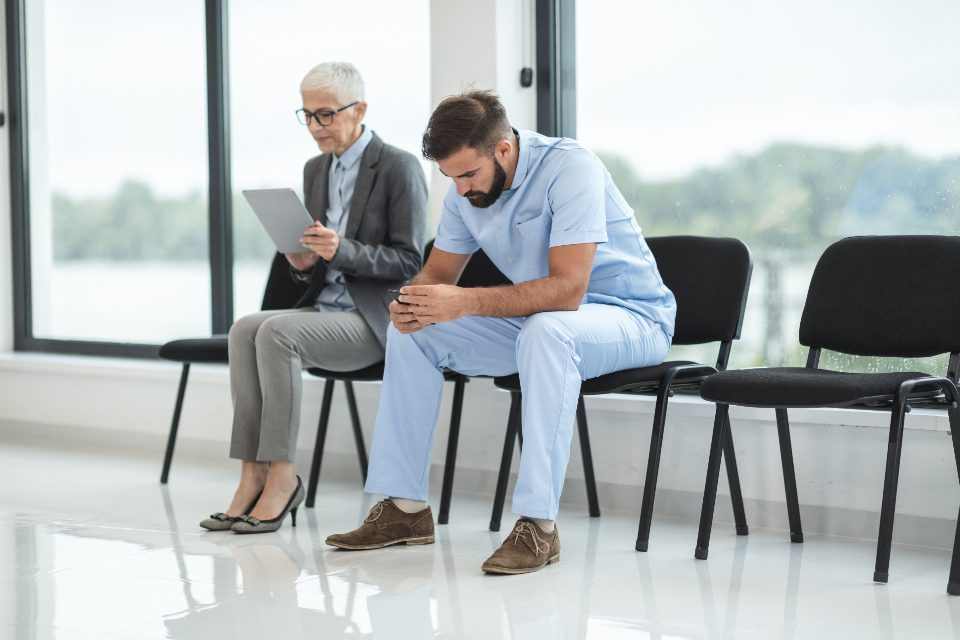 A hospital waiting room: a patient reading, a clinician slumped forward on a chair